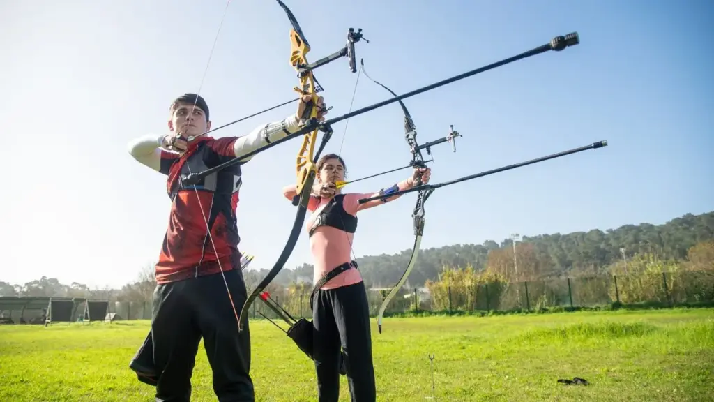 Zwei Bogenschützen mit Recurve-Bögen auf einer Wiese beim Training