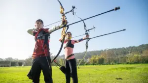 Zwei Bogenschützen mit Recurve-Bögen auf einer Wiese beim Training