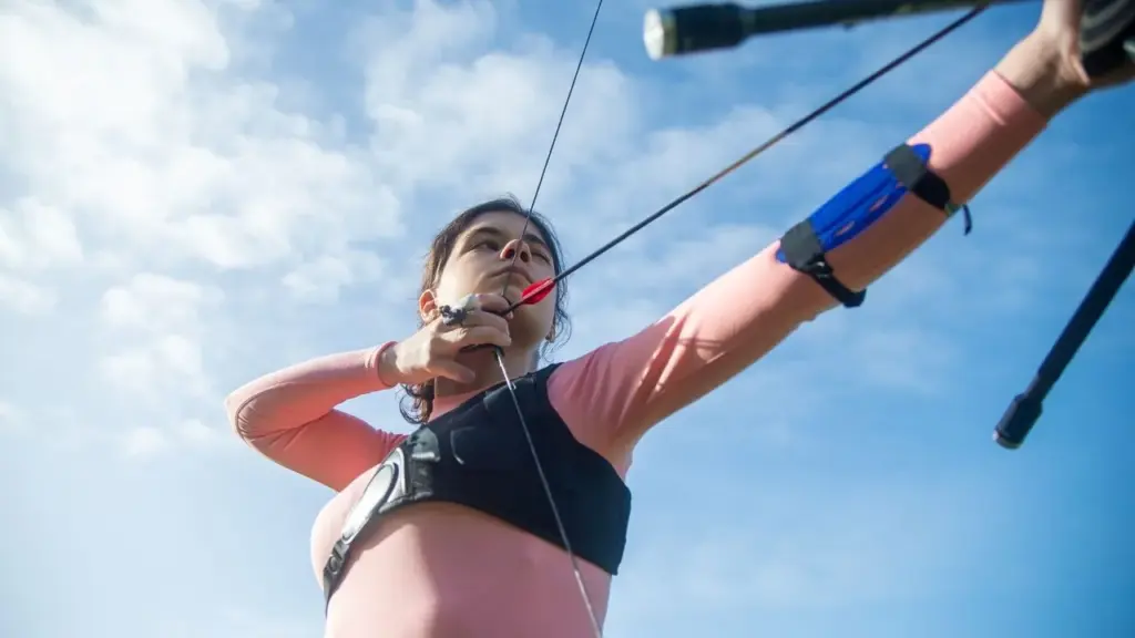 Junge Frau im Vollauszug mit Recurvebogen und Armschutz vor blauem Himmel